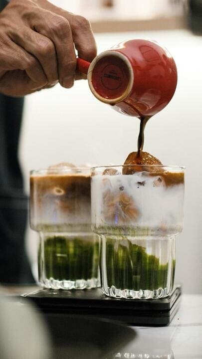 Barista pouring espresso into a signature layered matcha coffee