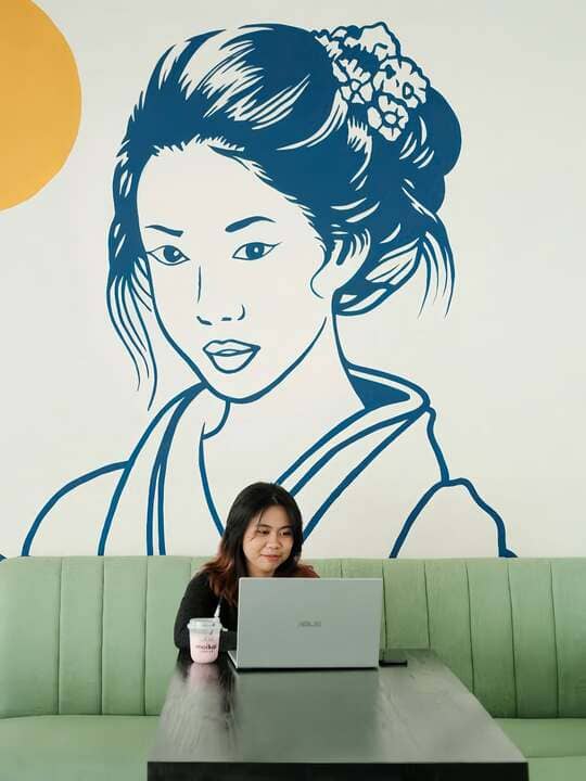 Customer working on laptop in front of Japanese art mural